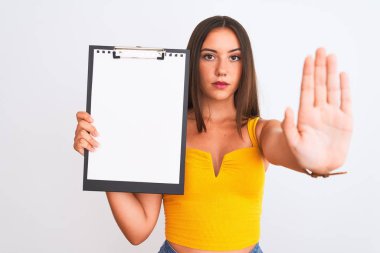 Young beautiful girl holding clipboard standing over isolated white background with open hand doing stop sign with serious and confident expression, defense gesture