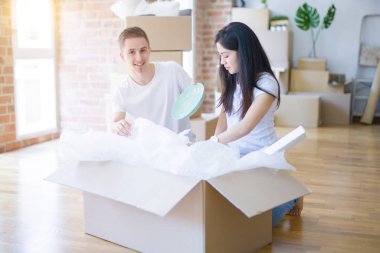 Young beautiful couple sitting on the floor at new home around cardboard boxes celebrating surprised and amazed for success with arms raised and open eyes. Winner concept.