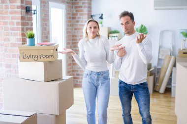 Karton kutuların etrafında duran genç ve güzel bir çift, elleri ve kolları havada, kafası karışmış bir ifade takınıyorlar. Şüphe kavramı.