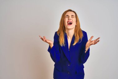 Redhead caucasian business woman wearing a suit over isolated background celebrating mad and crazy for success with arms raised and closed eyes screaming excited. Winner concept