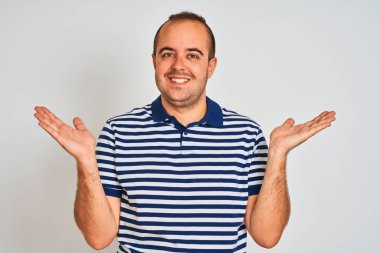 Young man wearing casual striped polo standing over isolated white background smiling showing both hands open palms, presenting and advertising comparison and balance