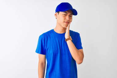 Çinli teslimatçı mavi tişört ve kep giyerek izole edilmiş beyaz arka planda duruyor diş ağrısı ya da diş ağrısı yüzünden ağız ve acı dolu bir ifadeyle dokunuyor. Dişçi konsepti.