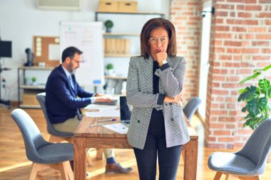 Middle age beautiful businesswoman wearing jacket and glasses standing at the office thinking looking tired and bored with depression problems with crossed arms. clipart