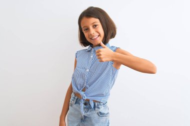 Genç, güzel, mavi gömlekli bir kız çocuğu izole edilmiş beyaz arka planda durup mutlu bir el hareketi yapıyor. Kameraya bakıp başarıyı gösteren ifade onaylanıyor.