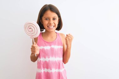 Güzel çocuk lolipop yiyor. İzole edilmiş beyaz arka planda duruyor. Gururla bağırıyor, zaferi kutluyor ve başarıyı kutluyor.