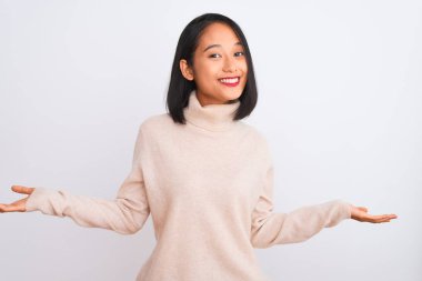Young chinese woman wearing turtleneck sweater standing over isolated white background smiling showing both hands open palms, presenting and advertising comparison and balance