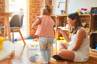 Güzel öğretmen ve sarışın öğrenci çocuk anaokulunda dinozorlarla oynuyor.