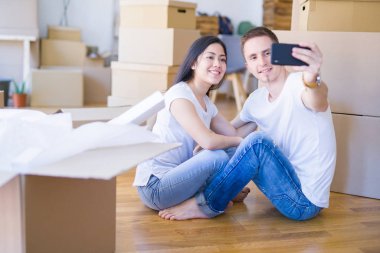 Young beautiful couple sitting on the floor at new home around cardboard boxes celebrating surprised and amazed for success with arms raised and open eyes. Winner concept.
