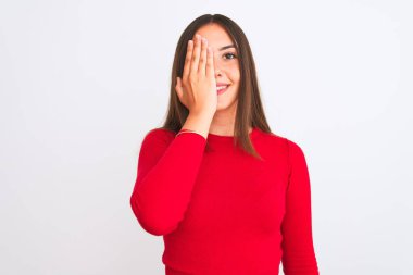 Young beautiful girl wearing red casual t-shirt standing over isolated white background covering one eye with hand, confident smile on face and surprise emotion.