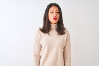 Beautiful chinese woman wearing turtleneck sweater standing over isolated white background looking at the camera blowing a kiss on air being lovely and sexy. Love expression.