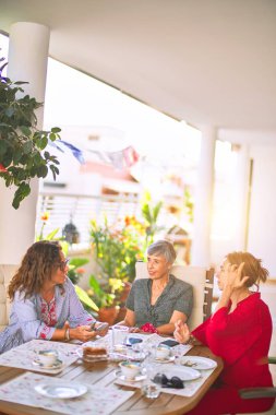 Orta yaşlı kadınlarla buluşup, öğle yemeği yiyip, kahve içiyorlar. Olgun arkadaşlar mutlu bir şekilde gülümsüyor. Güneşli bir günde evde akıllı telefon kullanıyorlar.