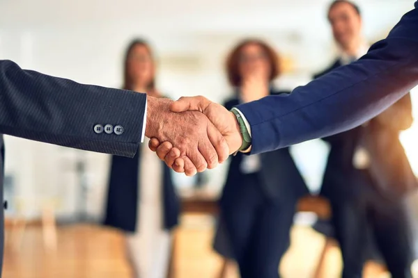 Group of business workers smiling happy and confident. Two of them, standing with smile on face shaking hands for agreement. Partners applauding at the office.