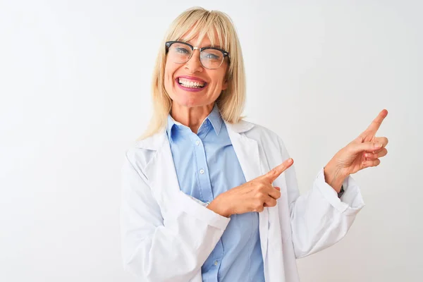 中年妇女科学家戴眼镜站在孤立的白色背景上 微笑着看着摄像机 用双手和手指指向侧面 — 图库照片