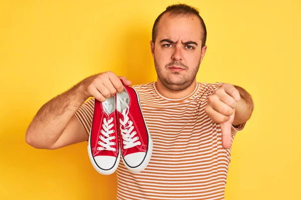 Young Man Holding Red Casual Sneakers Standing Isolated Yellow Background — 스톡 사진