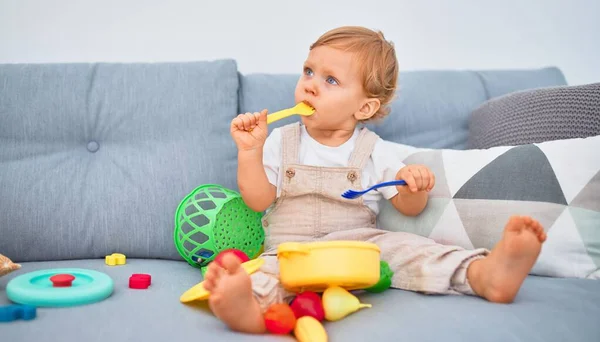 Sevimli Sarışın Çocuk Kanepede Oturup Evde Plastik Yemek Oyuncaklarıyla Oynuyor — Stok fotoğraf