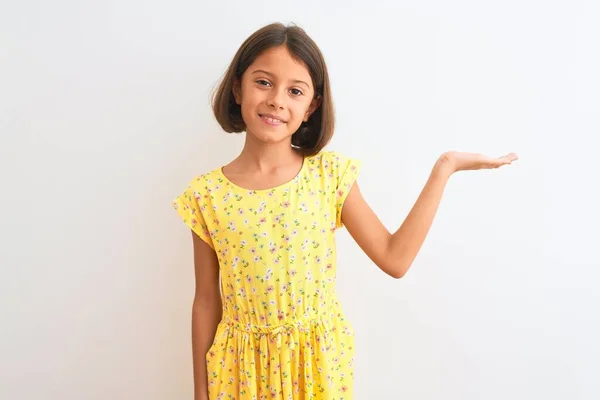 年轻美丽的小女孩穿着黄色的花衣 站在孤独的白色背景上 高兴地微笑着 手指手画脚地看着摄像机 — 图库照片