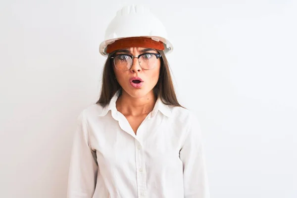 年轻美丽的建筑师女人 戴着头盔和眼镜 站在孤独的白色背景上 惊讶的表情 兴奋的脸 — 图库照片
