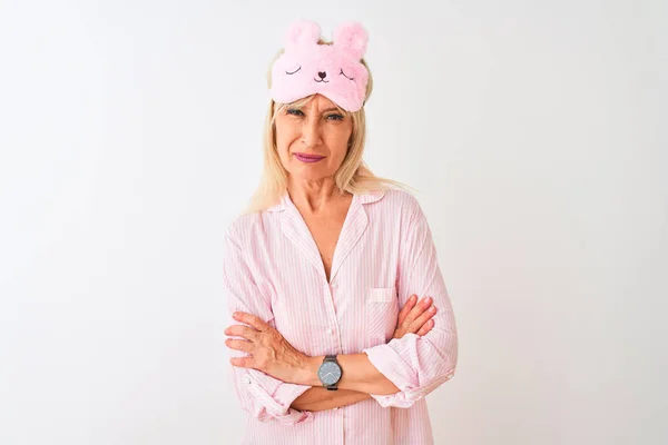 Middle age woman wearing sleep mask and pajama over isolated white background skeptic and nervous, disapproving expression on face with crossed arms. Negative person.