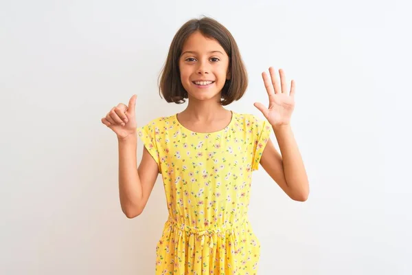 身穿黄色花裙的年轻漂亮的小女孩站在孤零零的白色背景上 带着六号手指指尖 自信而快乐地微笑着 — 图库照片