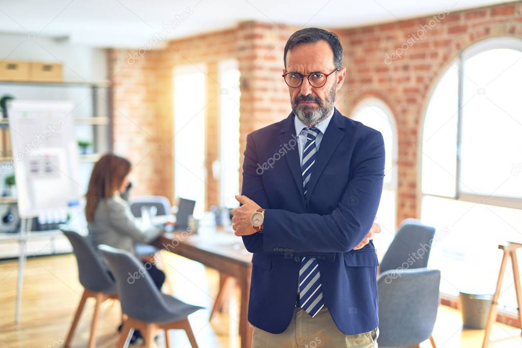 Middle age handsome businessman wearing glasses   standing at the office skeptic and nervous, disapproving expression on face with crossed arms. Negative person.