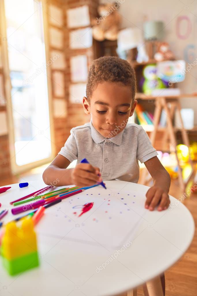 Beautiful african american toddler drawing using paper and marker pen at kindergarten