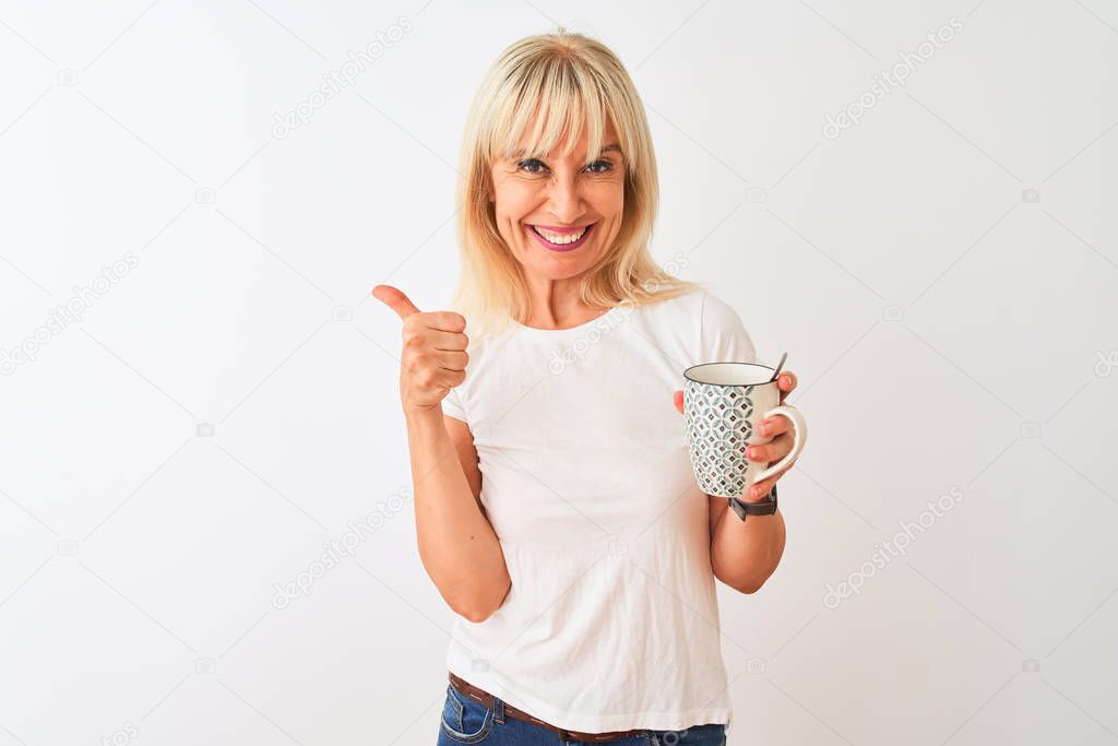 Middle age woman drinking cup of coffee standing over isolated white background happy with big smile doing ok sign, thumb up with fingers, excellent sign