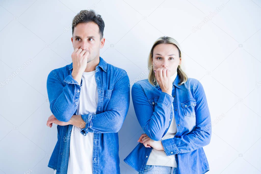 Young beautiful couple wearing denim shirt standing over isolated white background looking stressed and nervous with hands on mouth biting nails. Anxiety problem.