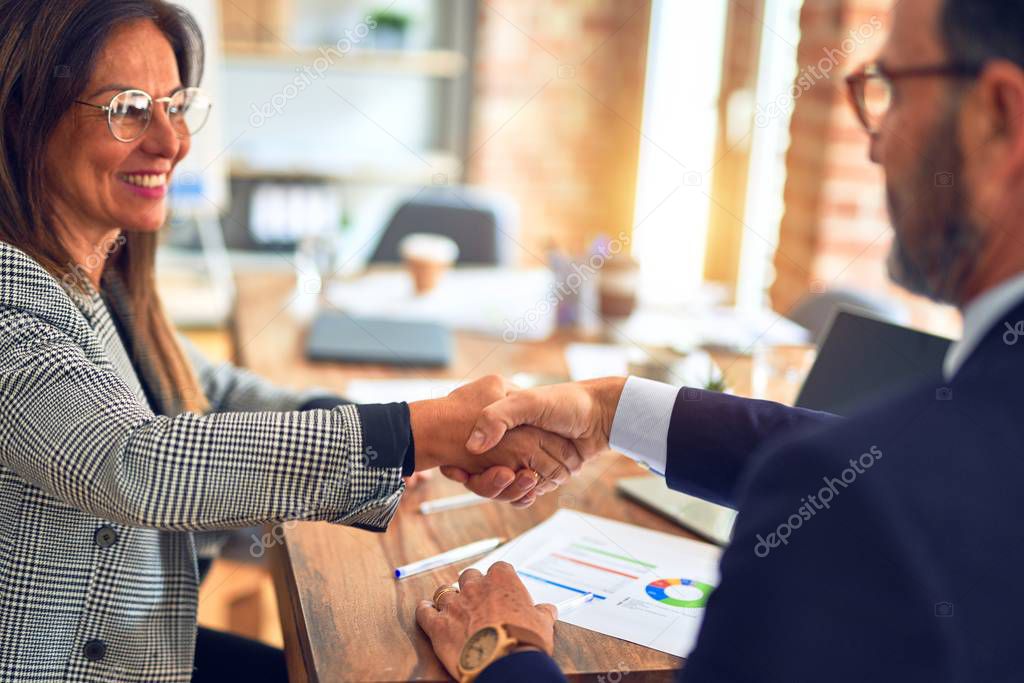 Two middle age business workers smiling happy and confident. Working together with smile on face shaking hands at the office