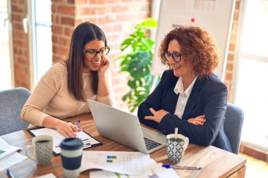 Two beautiful businesswomen smiling happy and confident. Sitting with smile on face working together using laptop at the office