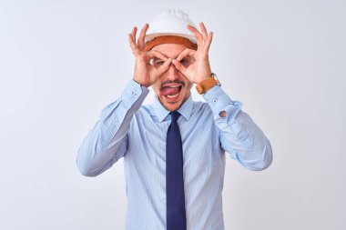 Müteahhit kaskı takan genç bir iş adamı izole edilmiş arka planda dürbün gibi jest yapıyor. Dürbün dili dışarı çıkarıyor, gözler parmaklarından bakıyor. Çılgın ifade.