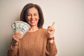 Středního věku brunetka žena drží jeden dolar bankovky přes izolované pozadí velmi šťastný ukazující rukou a prstem na stranu