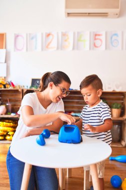 Güzel öğretmen ve küçük çocuk anaokulunda klasik mavi telefonla oynuyor.