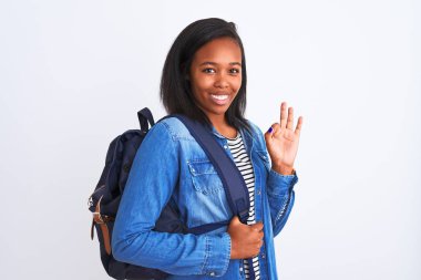 Tecrit edilmiş arka planda sırt çantası takan Afro-Amerikan genç bayan. Tamam işareti yapıyor, mükemmel bir sembol.