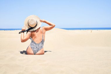 Genç ve güzel bir kadın kumsalda güneşleniyor. Maspalomas kumullarında eşofman giyiyor.