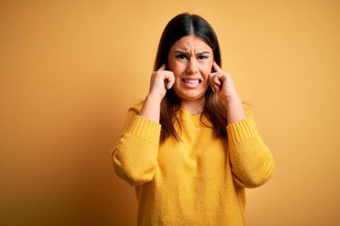 Sarı arka plan üzerine günlük süveter giyen genç ve güzel bir kadın yüksek sesli müzik sesi için kulakları parmaklarıyla kapatıyor. Sağır kavramı.