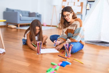 Anaokulundaki bir sürü oyuncağın etrafında kalem ve kağıt kullanarak güzel bir öğretmen ve bebek resmi çiziyor.