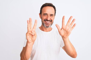 İzole edilmiş beyaz arka plan üzerinde duran orta yaşlı yakışıklı bir adam 8 numaralı parmaklarıyla gülümseyerek kendinden emin ve mutlu bir şekilde duruyor..