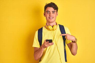 Teenager boy wearing headphones and using smartphone over isolated background very happy pointing with hand and finger