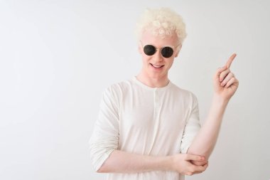 İzole edilmiş beyaz arka planda güneş gözlüğü ve tişört giyen genç, albino sarışın adam zafer işareti yaparken kameraya gülümsüyor. İki numara..