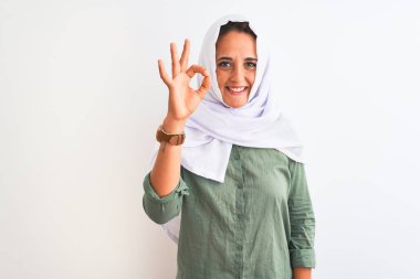 Geleneksel Müslüman tesettürlü genç, güzel bir Arap kadın izole edilmiş arka planda gülümsüyor ve el ve parmaklarıyla 