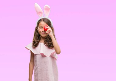 Esmer Latin kız ayakta ve diş gösterilen kendine güvenen bir gülümsemeyle gülümseyerek mutlu bir yüz ile Paskalya tavşan kulakları giyiyor