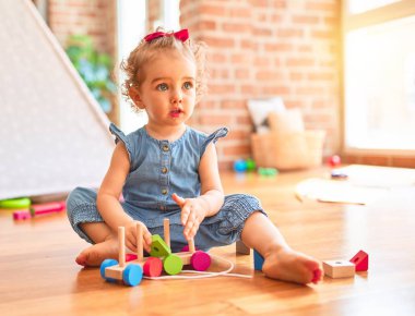 Renkli oyun odasında beyaz güzel bir bebek oyuncaklarla oynuyor. Anaokulundaki ahşap tren parçalarıyla mutlu ve eğlenceli..