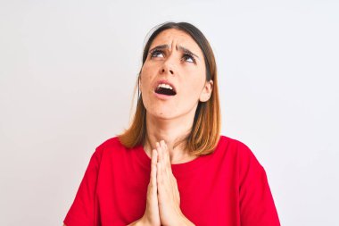Beautiful redhead woman wearing casual red t-shirt over isolated background begging and praying with hands together with hope expression on face very emotional and worried. Asking for forgiveness. Religion concept.