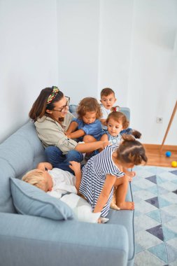 Güzel öğretmen ve bir grup çocuk kanepede oturup anaokulunda oynuyorlar.