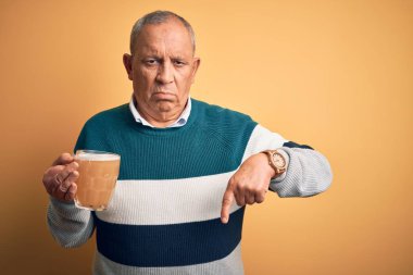 Üst düzey yakışıklı adam izole edilmiş sarı arka planda duran bira kavanozunu içiyor üzgün ve üzgün görünüyor, parmaklarıyla yönü gösteriyor, mutsuz ve depresif..