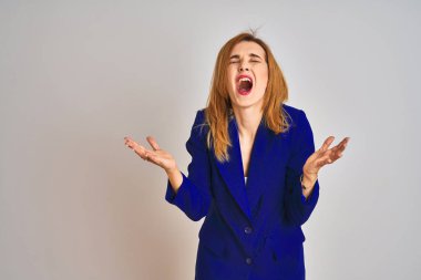 Redhead caucasian business woman wearing a suit over isolated background crazy and mad shouting and yelling with aggressive expression and arms raised. Frustration concept.