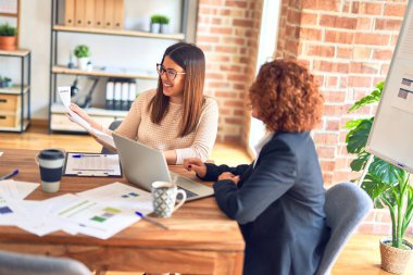 Two beautiful businesswomen smiling happy and confident. Sitting with smile on face working together using laptop at the office