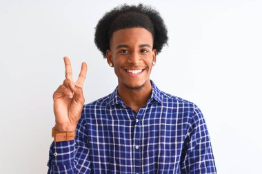 Genç Afro-Amerikan erkek, günlük gömlekler giyip izole edilmiş beyaz arka planda dikiliyor. Kameraya gülümsüyor ve zafer işareti yapıyor. İki numara..