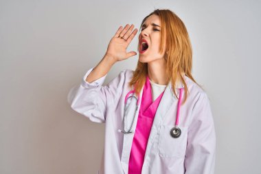 Redhead caucasian doctor woman wearing pink stethoscope over isolated background shouting and screaming loud to side with hand on mouth. Communication concept.