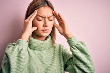 Pembe izole edilmiş arka plan üzerine kışlık yün kazak giyen genç güzel sarışın kadın acı ve migren yüzünden çaresiz ve stresli bir baş ağrısı çekiyor. Ellerini başının üstüne koy..